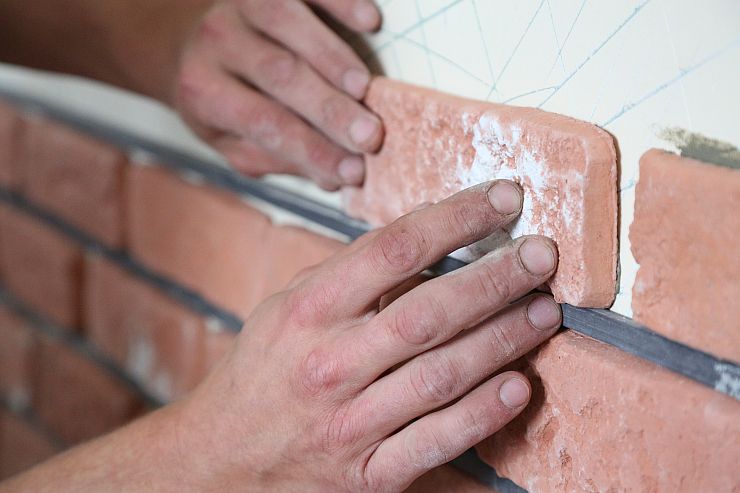 Zwei Hände verlegen Klinkerriemchen mit Klinkermörtel - präzises Auftragen für eine gleichmäßige Fassade